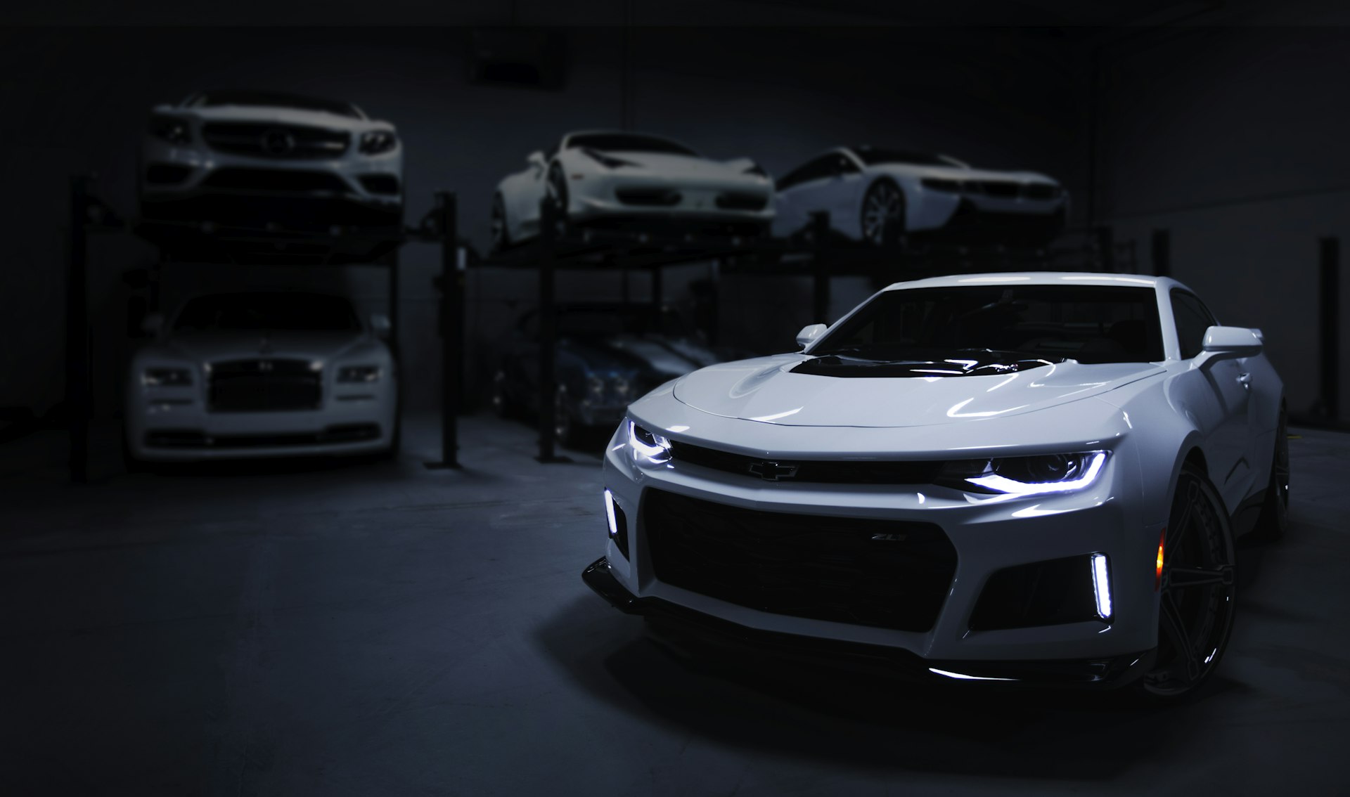 Premium vehicles parked in a dark showroom garage.